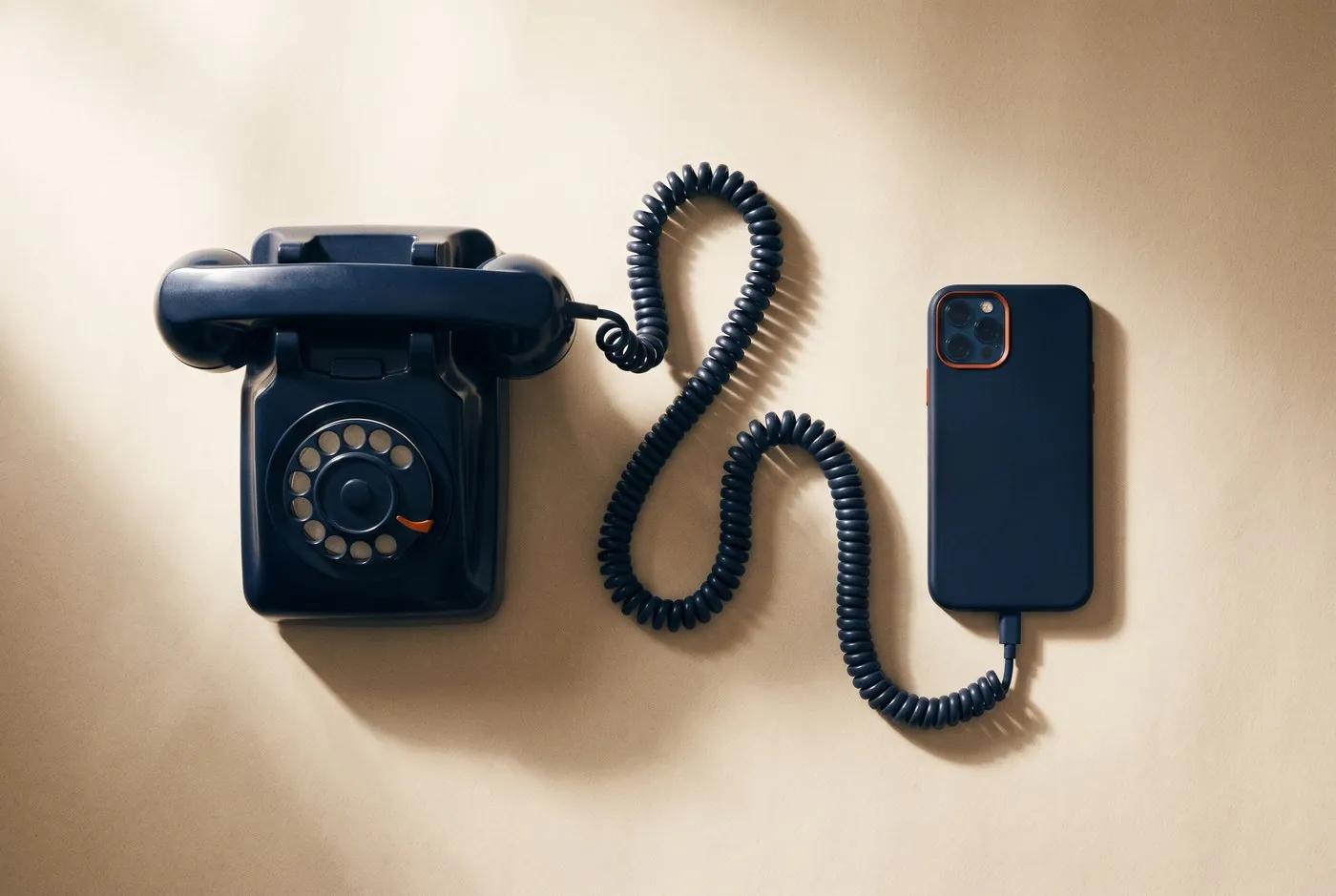 Um telefone de disco azul-marinho conectado por um fio espiralado a um smartphone moderno, sobre fundo bege.